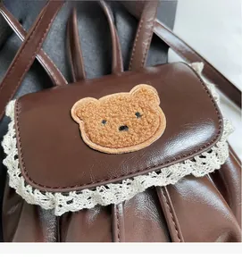 Close-up of vintage brown leather bag with lace trim and cute plush bear patch
