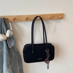 Close-up of black suede shoulder bag featuring gold logo lettering and decorative knot detail