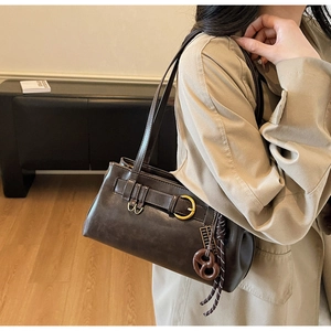Détail du sac sous le bras en cuir marron foncé avec boucle dorée et breloque bretzel