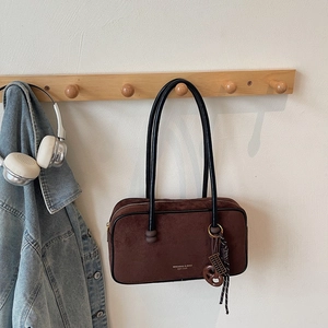 Detail of coffee suede tote bag with brand print and woven charm on a wooden wall hook