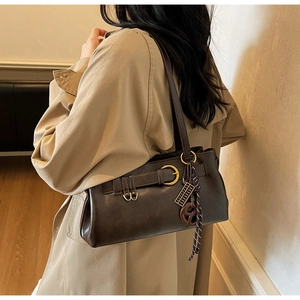 Sac sous le bras marron foncé avec détails dorés porté sur un trench-coat chic
