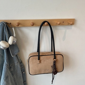 Detail view of beige suede shoulder bag with black tubular handles and gold logo text