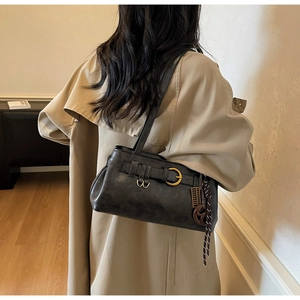 Détail d'un sac bandoulière noir vintage avec boucle dorée sur un trench-coat kaki
