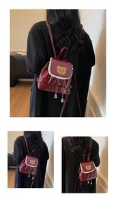 Close-up of wine red mini backpack featuring white lace trim and cute brown bear patch