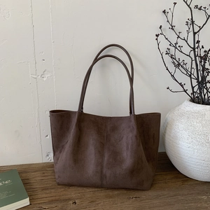 Detail of a dark brown suede tote bag with a vertical seam on a minimalist wooden table