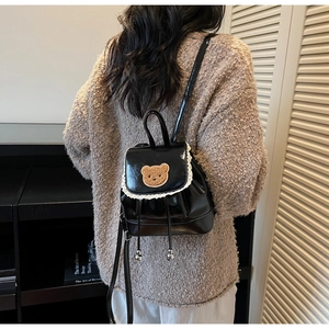 Detail of black glossy mini backpack with beige lace trim and cute brown bear patch