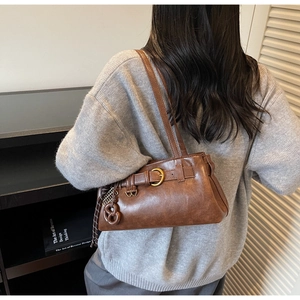 Détail d'un sac porté épaule vintage marron foncé avec boucles dorées porté par un mannequin
