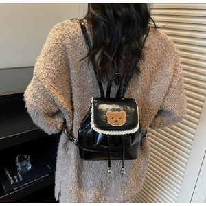 Detail of black glossy mini backpack featuring brown bear patch and white lace trim