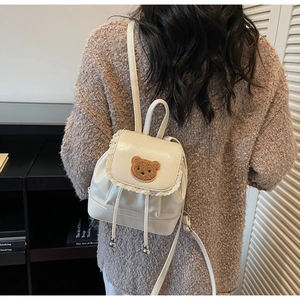 Close-up of cream PU leather backpack featuring lace edges and brown bear embroidery detail