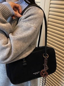 Minimalist black suede shoulder bag with long strap and creative pretzel charm pendant