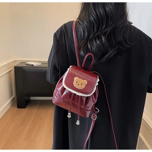 Close-up of a burgundy glossy PU mini backpack featuring a cute bear patch and lace trim