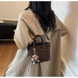 Borsa a secchiello marrone con ciondolo di peluche abbinata a un trench in stile autunnale