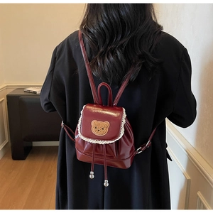 Detail of dark red patent leather bag featuring lace trim and a cute plush bear patch