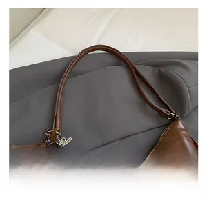 Detail view of brown glossy leather shoulder bag with plush charm and metal tag