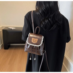 Detail of a brown mini backpack with white lace edges and a cute plush bear patch
