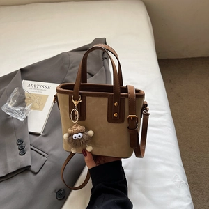 Dettaglio borsa a secchiello kaki con manici in pelle marrone e charm a mostriciattolo