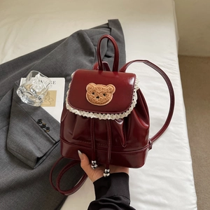 Close-up of a burgundy mini backpack with white lace trim and a cute plush bear patch