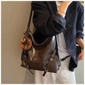 Detail of a large brown vintage tote bag with metal logo and cute donut charm accessory