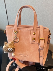 Borsa a secchiello rosa opaco con rivetti, dettagli in bronzo e ciondolo a mostriciattolo