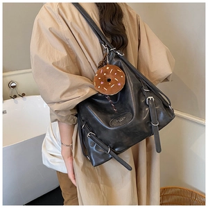 Detail of a black leather tote bag featuring metal buckles and a donut plush pendant charm