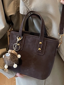 Borsa a secchiello minimalista marrone scuro con ciondolo peluche e logo inciso