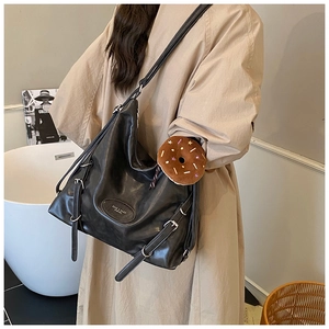 Detail of black tote bag with silver buckles and a cute donut plush charm on the strap