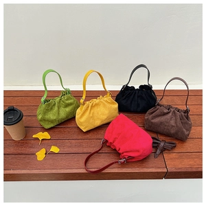 Detail of five pleated suede tote bags in various colors displayed on a wooden bench