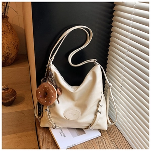 Detail of cream hobo bag with donut plush pendant on wooden surface under soft blinds light