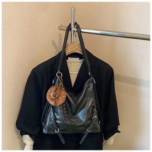Detailed macro view of black faux leather tote bag with silver buckles and a donut charm