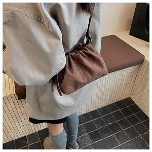 Detail of dark brown suede drawstring bag with pleated texture and thin shoulder strap