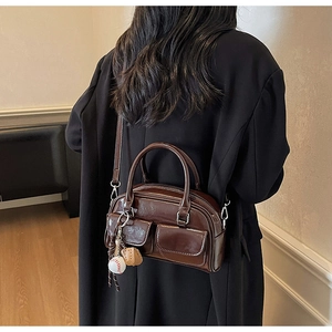 Detail view of a glossy dark brown Boston bag with baseball charms on a black coat