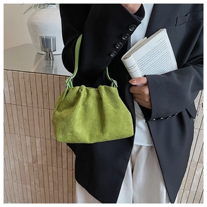 Detail view of grass green suede ruched handbag with slim handle on model outfit