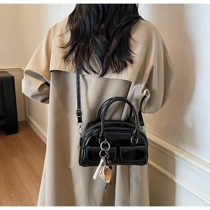Detail of a shiny black patent mini Boston bag worn with a khaki trench coat