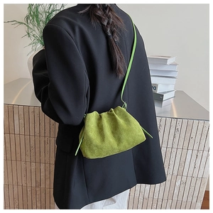 Detail view of a green pleated suede cloud bag with a slim shoulder strap worn on a black blazer