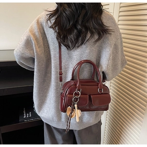 Model wearing a burgundy patent leather Boston bag with double front pockets and baseball charm