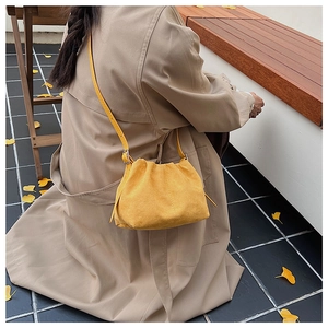 Detail of yellow faux suede pleated cloud bag worn by a model in an autumn setting
