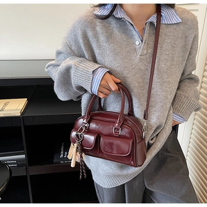 Detail of burgundy Boston bag with dual front pockets and baseball charm on a model
