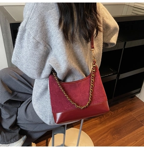 Detail of burgundy patchwork shoulder bag with gold chain strap on grey knitwear