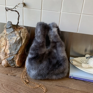 Detail of plush grey faux fur tote bag with golden metal chain strap on wooden table