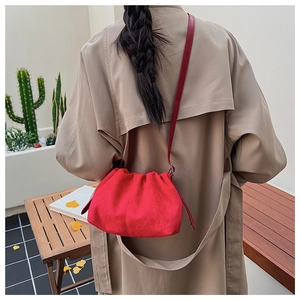 Detail of red suede cloud bag with pleated design and thin shoulder strap on model