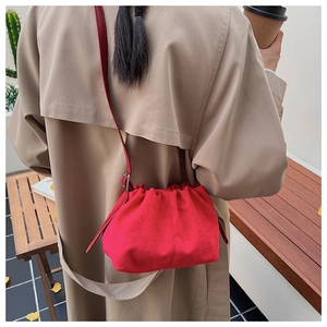 Detail view of red pleated suede crossbody bag worn with a beige trench coat in autumn