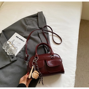 Detail of burgundy glossy leather Boston bag with dual pockets and baseball charm