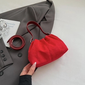 Detail of red pleated suede shoulder bag with detachable strap in lifestyle setting