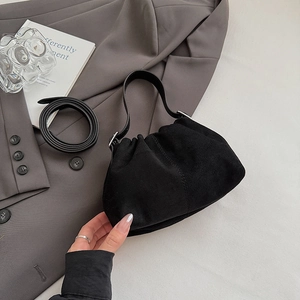 Detail of a minimalist black suede pleated handbag with smooth leather straps and silver buckle