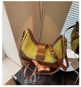 Detailed close-up of green suede and brown leather baguette bag with gold chain link