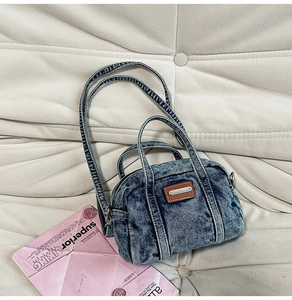 Detailed macro of washed blue denim Boston bag with leather tag on quilted sofa