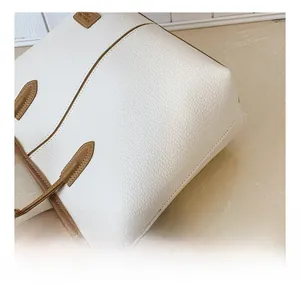Close-up of white lychee leather texture with brown edges and a plush bear charm