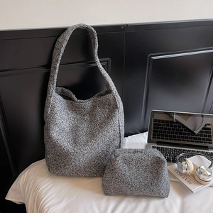 Détail du sac cabas en tissu bouclé gris avec pochette assortie posé sur un lit