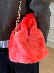 Faux fur handbag in bright red with gold chain strap worn by a model in casual style