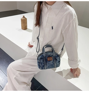Close-up of washed blue denim handbag with brown leather patch and dual zipper detail